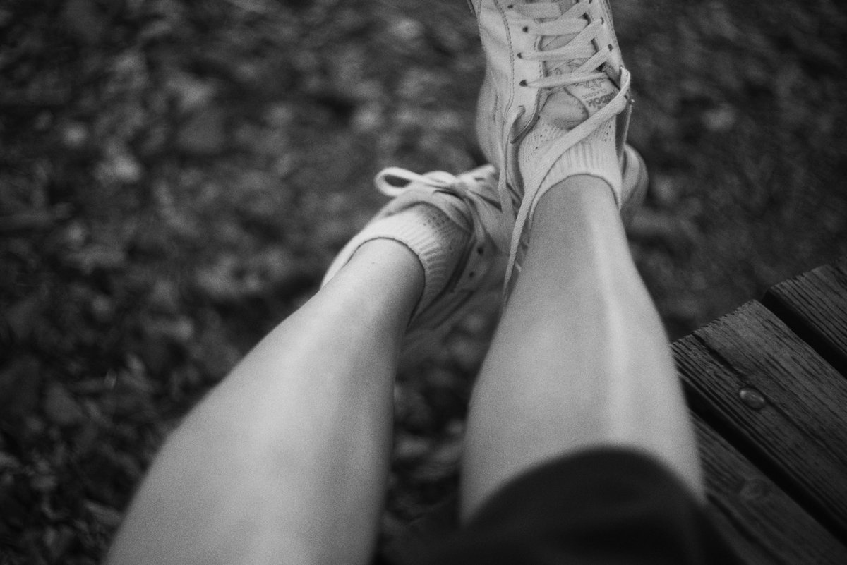 Jambes et baskets posées sur un banc en bois, en noir et blanc