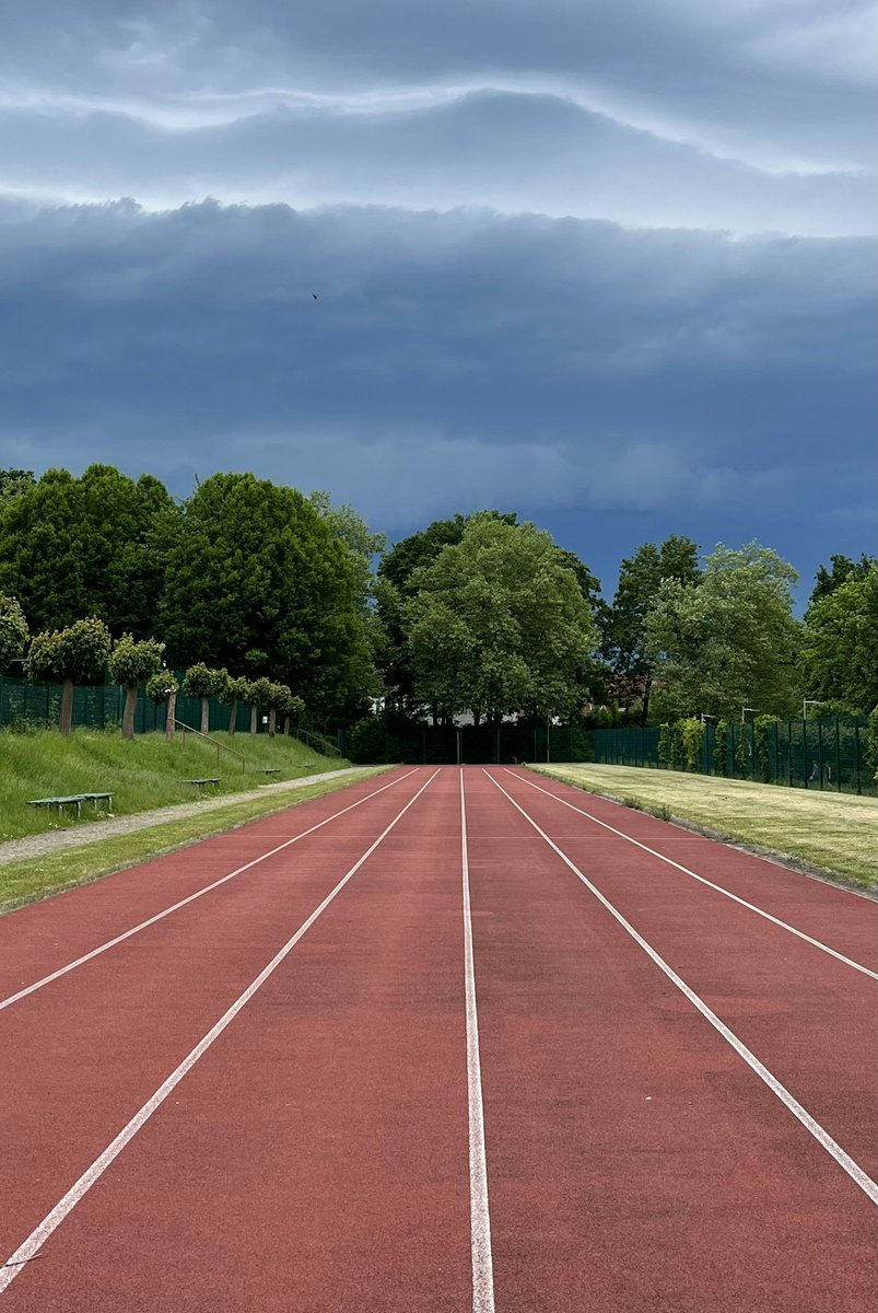 Piste d'athlétisme rouge bordée d'arbres sous un ciel d'orage